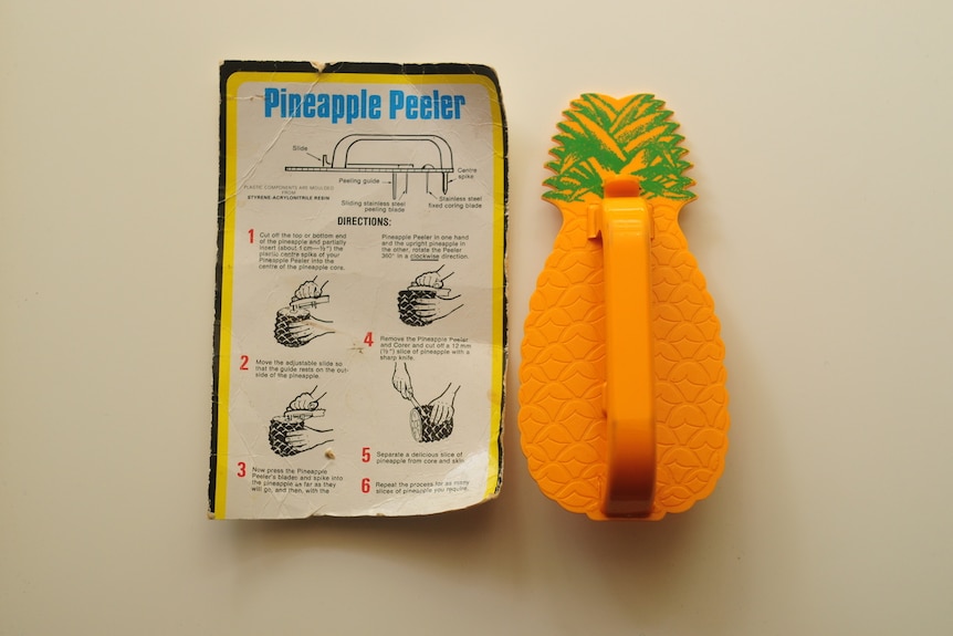 A bright yellow pineapple-shaped plastic cutter beside a piece of cardboard showing how to use the device.