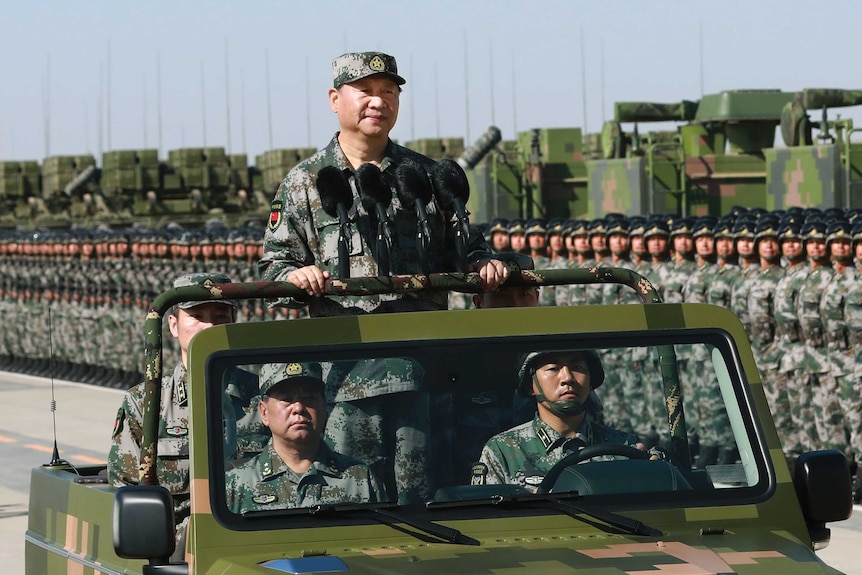 Chinese President Xi Jinping, dressed in camouflage gear, stands atop a military car during a parade.