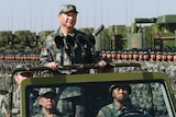 Chinese President Xi Jinping, dressed in camouflage gear, stands atop a military car during a parade.