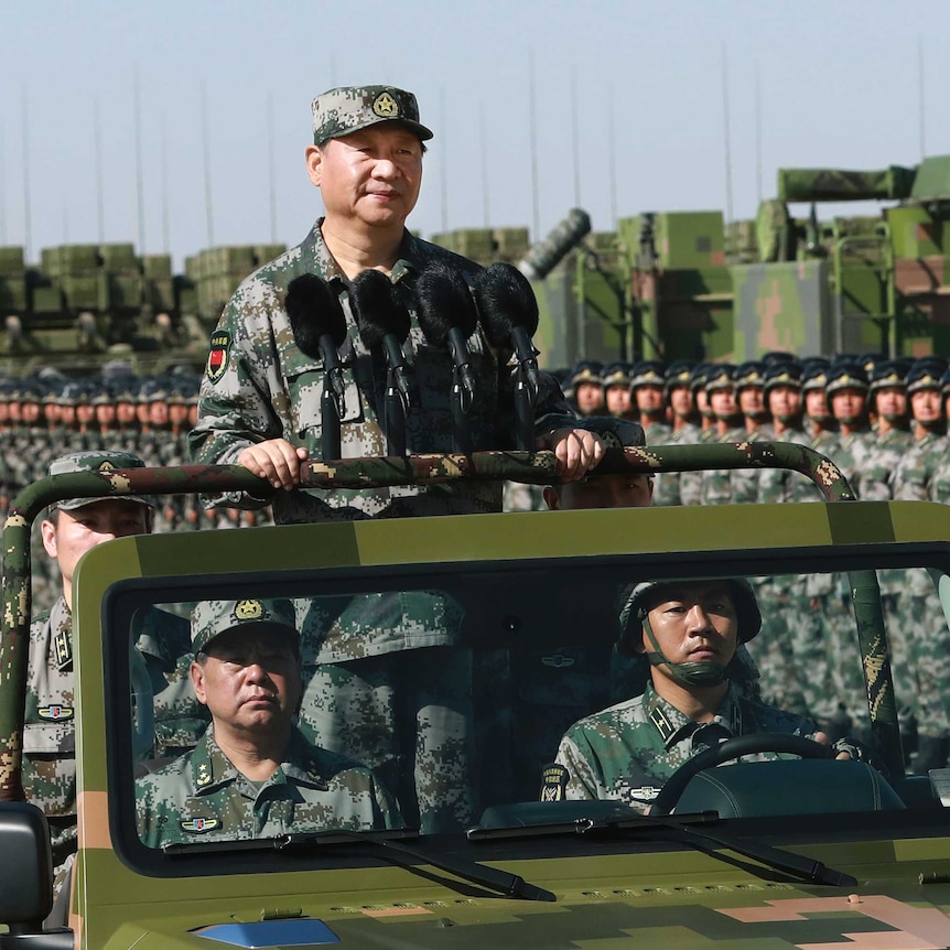 Chinese President Xi Jinping, dressed in camouflage gear, stands atop a military car during a parade.