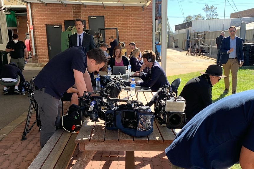 Group of journalists and camera crews with equipment set up on outside tables working.