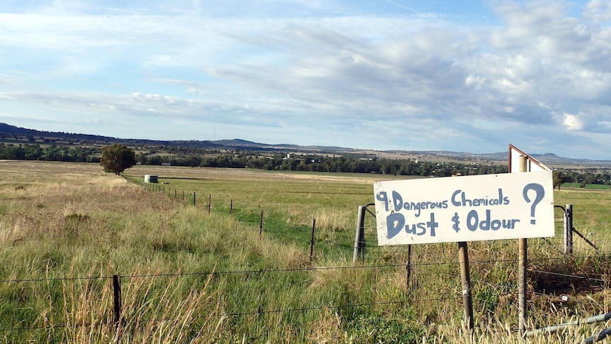 Green farming field with no development in sight except for protest sign along fencing.