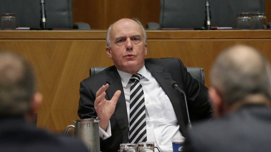 Eric Abetz sits in a leather chair questioning departmental officials with their back to the camera
