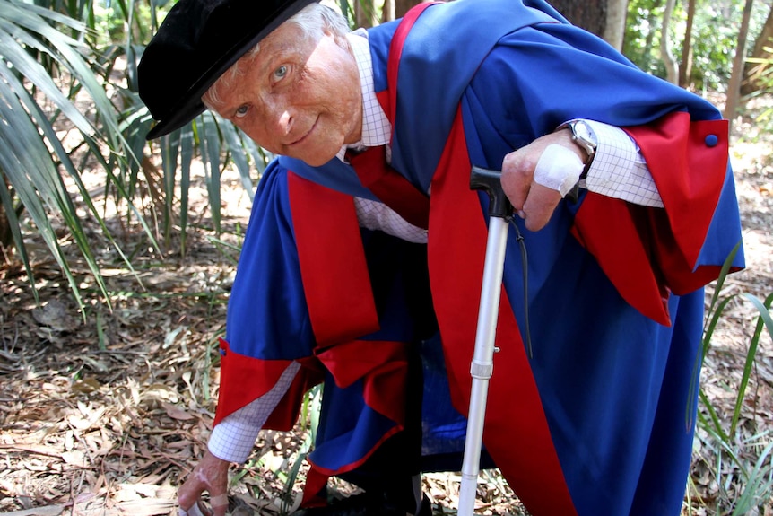 Dr Robert Sawyer crouches in bushland near Wollongong