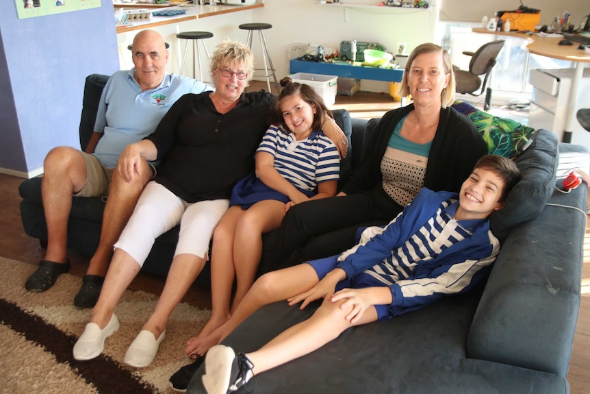 Ian, Irene and Kate sit with the kids Noah and Kayla on the family couch, an example of a multigenerational living arrangement
