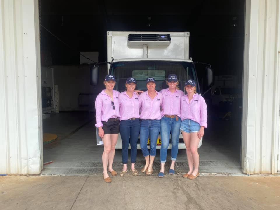 Five women stand in front of a truck wearing pink shirts