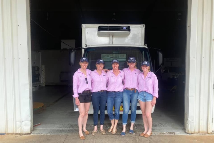 Five women stand in front of a truck wearing pink shirts