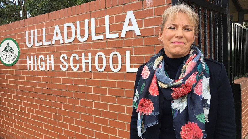 Ulladulla High School Principal, Denise Lofts standing at the front gate of her school with a school name on a brick fence