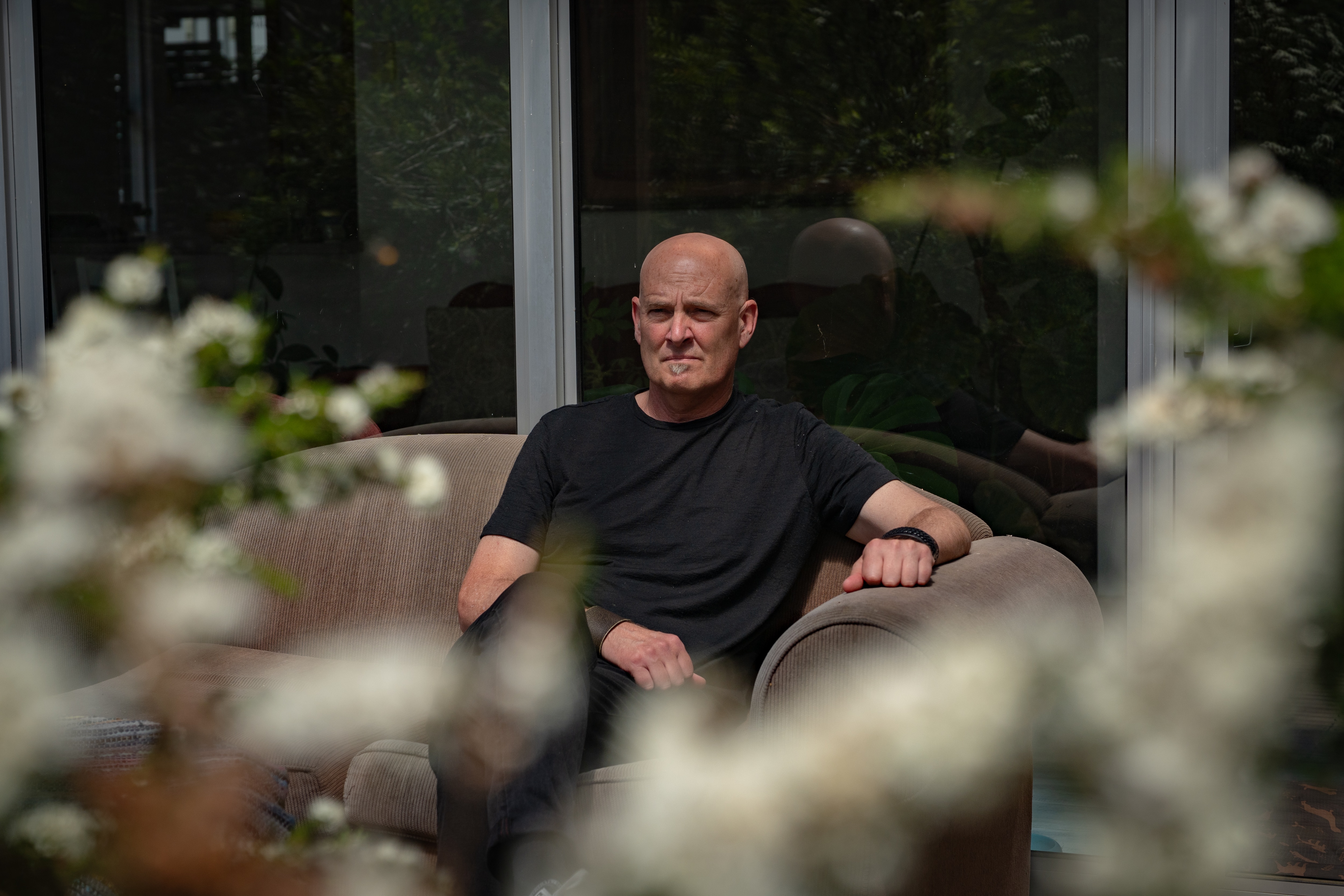 A man in a dark shirt sits outdoors near some native plants looking out into the distance