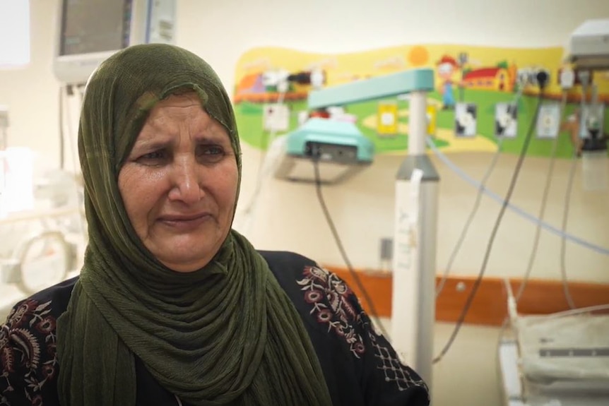 A woman wearing a headscarf cries while standing inside a hospital ward.