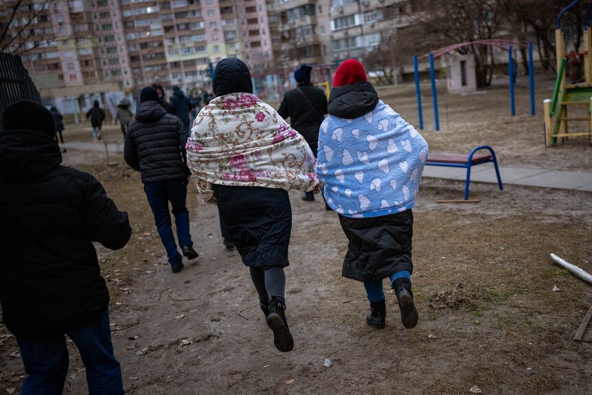 The backs of many people running towards a building for shelter.