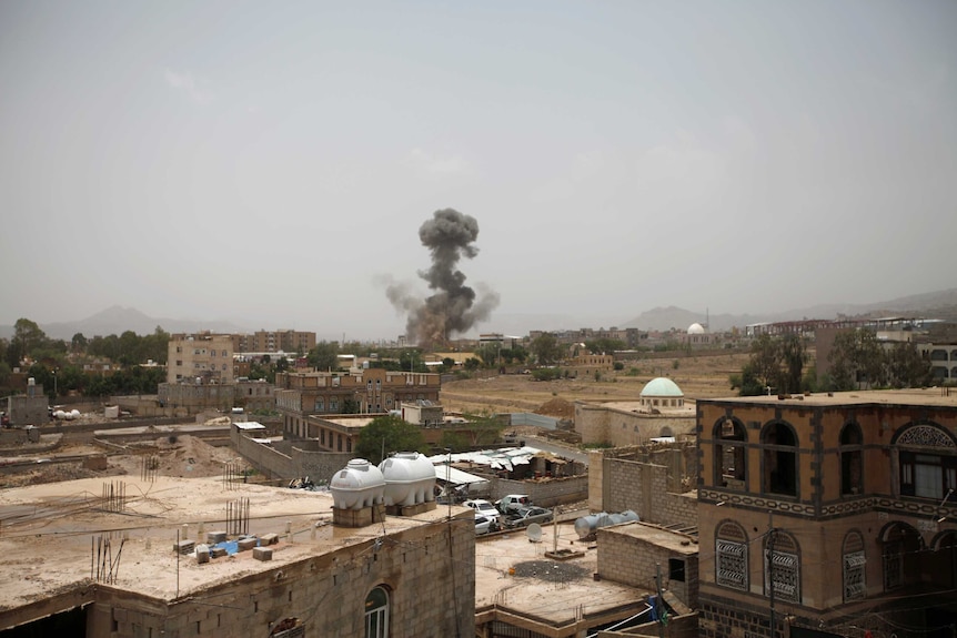 A long shot shows buildings and smoke rising in the distance.