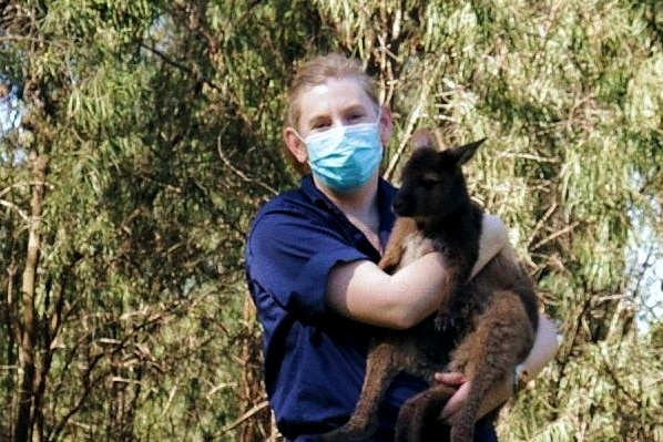 A masked woman holding a joey.