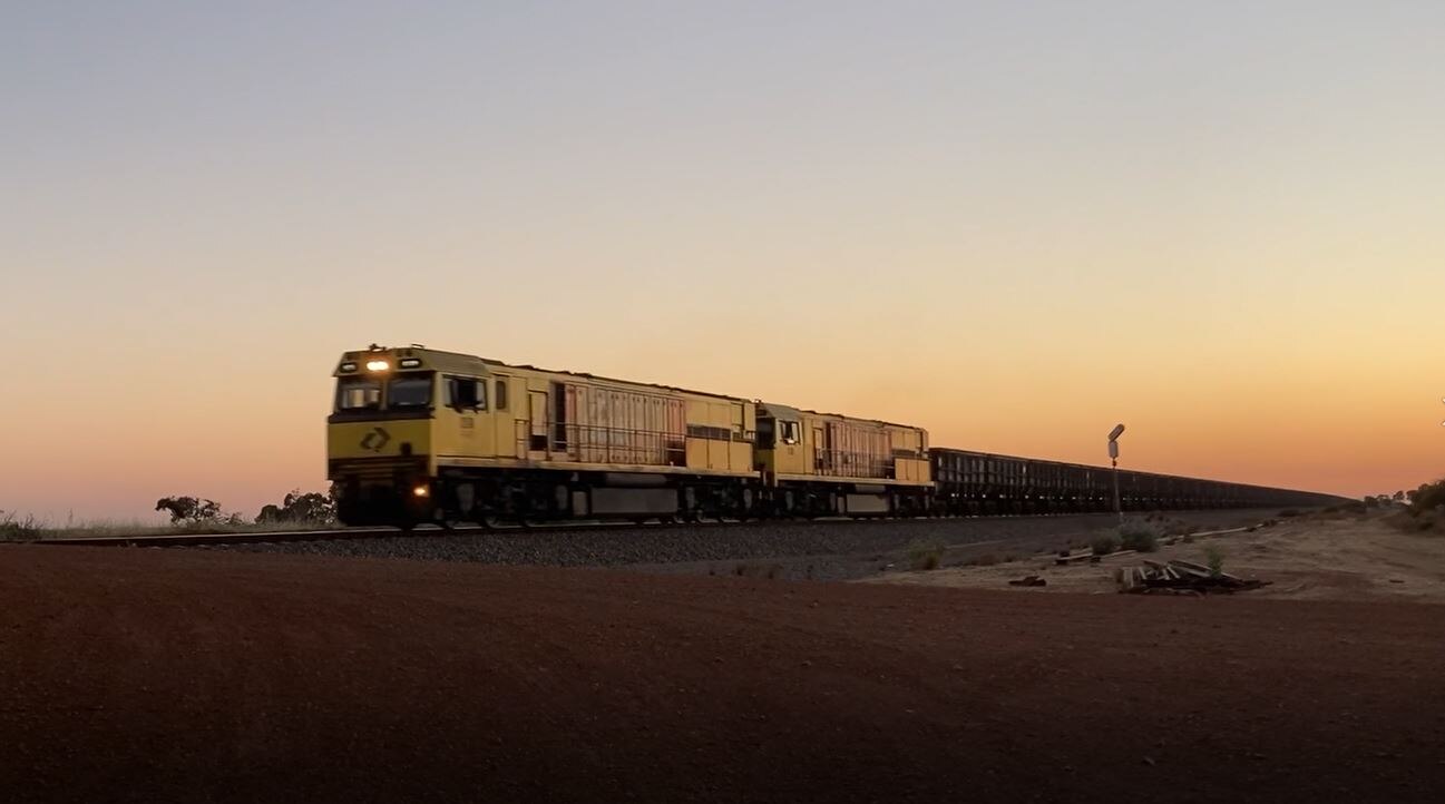 A freight train in low lights, crossing the desert.
