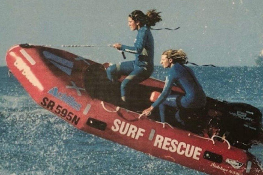Two women in wetsuits ride the waves in an inflatable rescue boat.