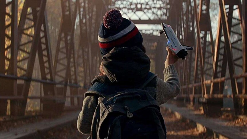 A young boy on a trestly bridge is holding up a spaceship figurine.