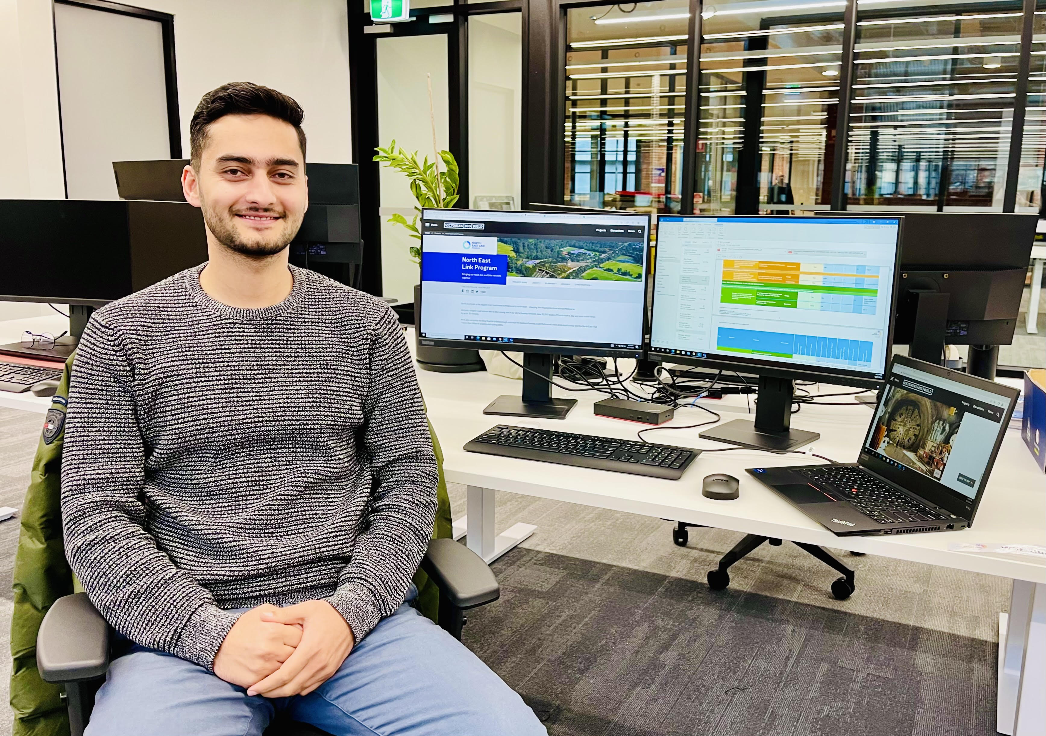 picture of a young man smiling in a chair in front of computers in an office