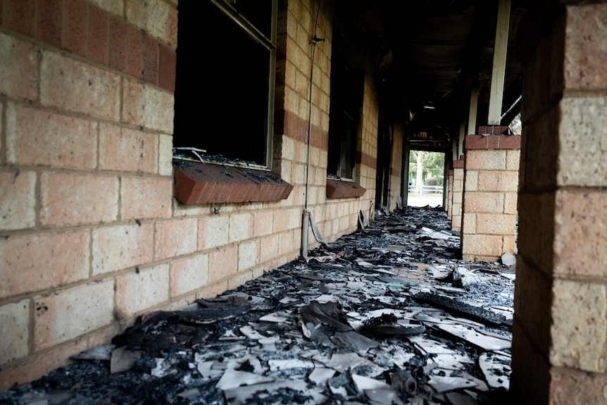 Charred ground on the porch of a home destroyed in a bushfire, with windows scorched and burnt out.