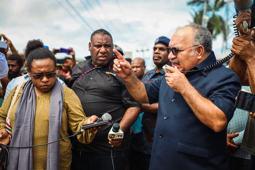 A man speaks into a megaphone surrounded by journalists outside in PNG