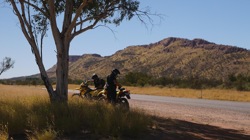 two police officers on dirt bikes sitting in the shade on a desert highway
