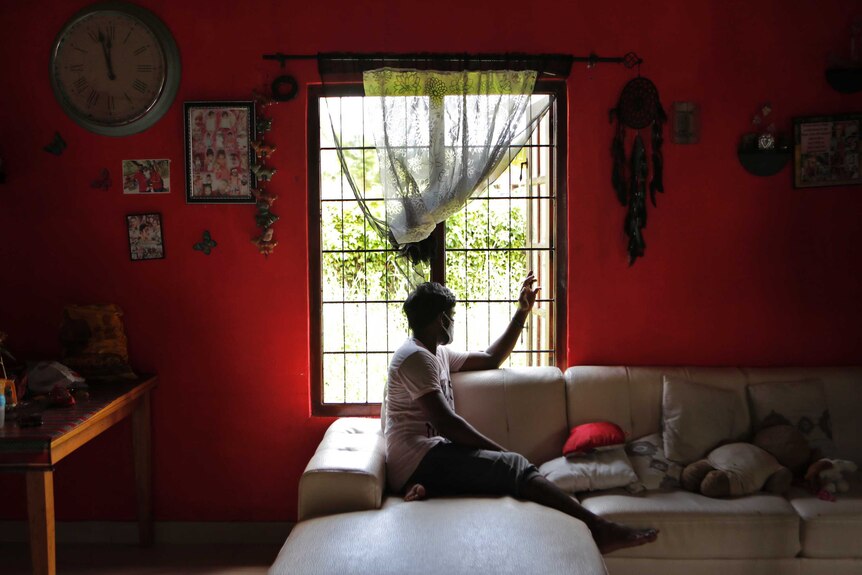 A man in a face mask looks out a window