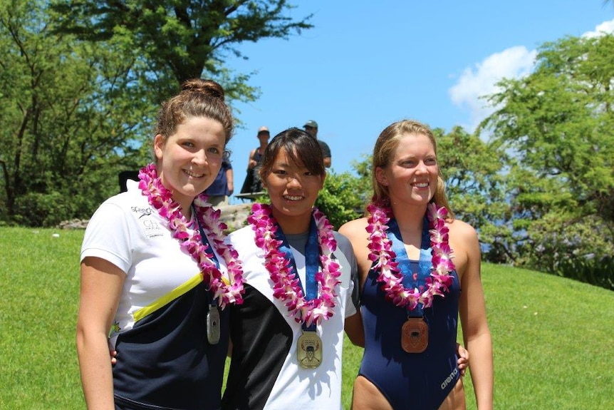 Three girls with swimming medals around their necks pose for a photo.