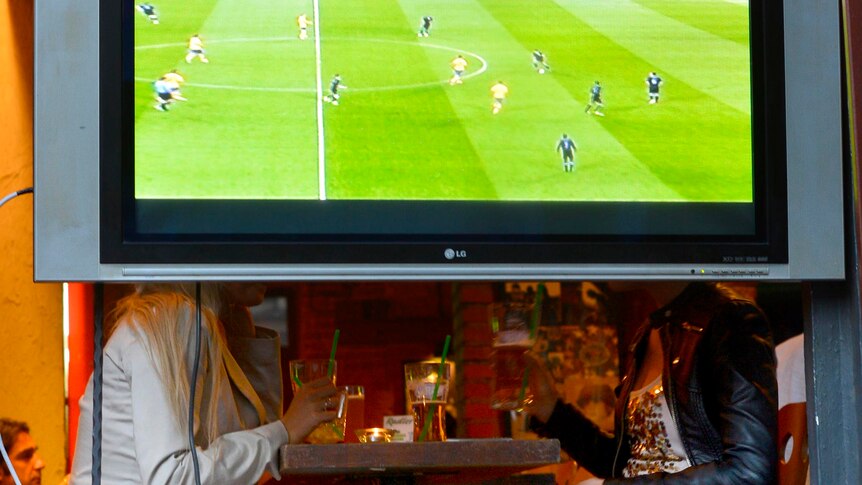 Two woman have a drink behind a TV during Euro 2012.