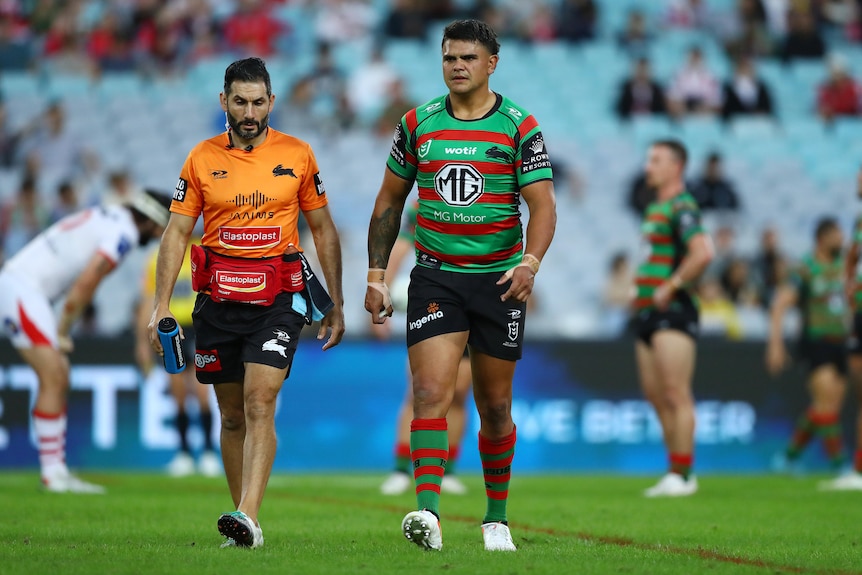 South Sydney NRL star Latrell Mitchell looks serious as he walks off the ground with a trainer during an NRL game. 