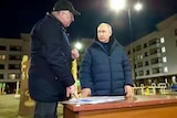 Vladamir Putin speaking to a man with paper on a desk outdoors