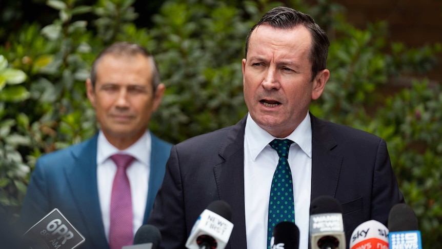 Mr McGowan speaks in front of a clutch of microphones, WA Health Minister Roger Cook looks on.