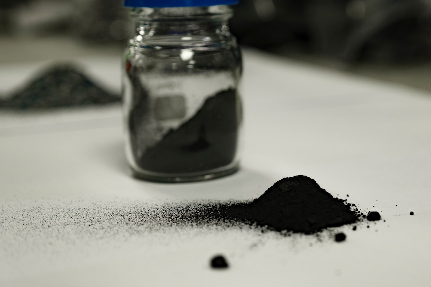 a powdery black substance on a white surface with a jar in the background.