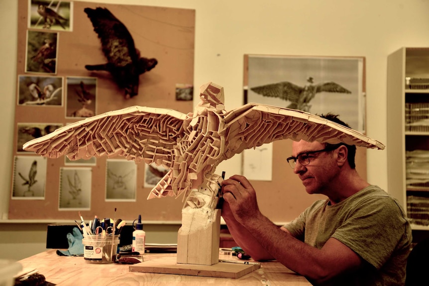 a man working on a model of a bird with its wings spread out