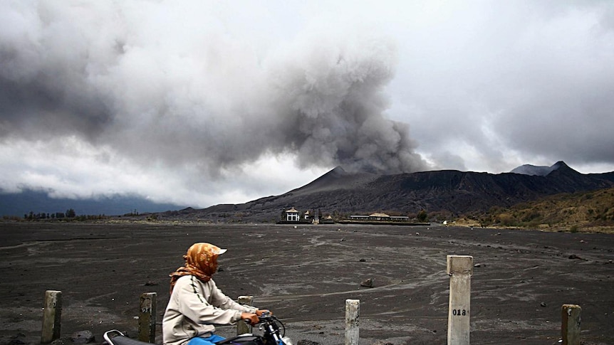 Motorcyclist passes by a smoking Mount Bromo volcano