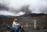 Motorcyclist passes by a smoking Mount Bromo volcano