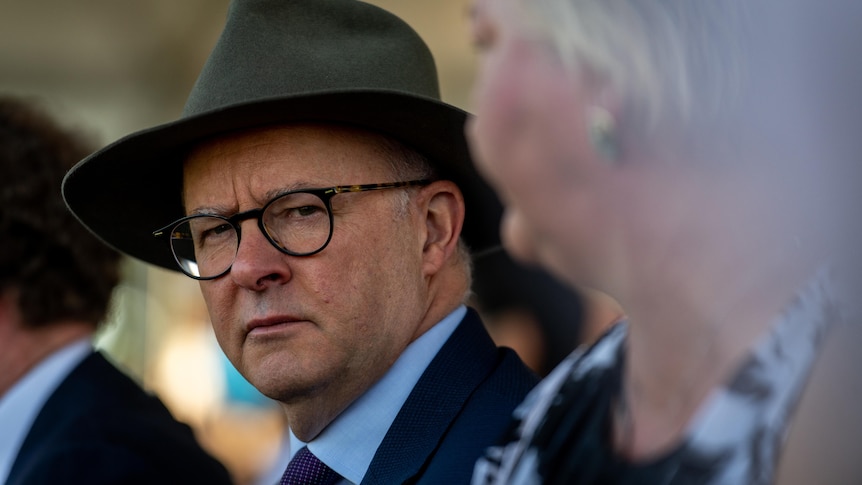 Anthony Alabanese in a wide brimmed hat looks toward the camera with a woman out of the focus in the foreground