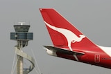 The tail of a Qantas plane featuring the iconic kangaroo logo passes a control tower at Sydney airport.