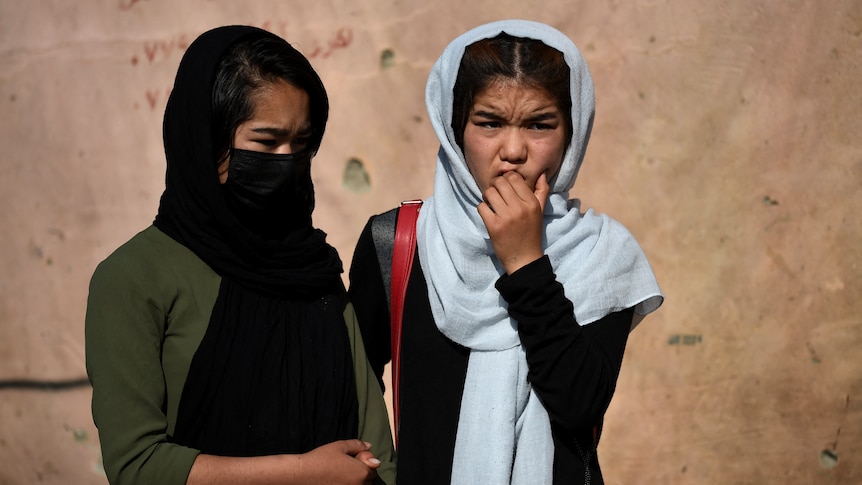 Two girls wearing headscarves stand outside a school