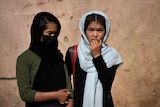 Two girls wearing headscarves stand outside a school