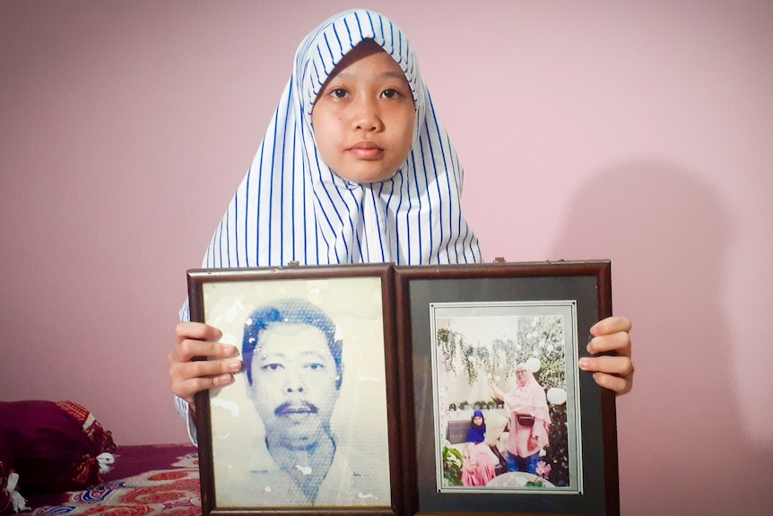 A little girl in a veil holds framed photographs of her late mother and father 