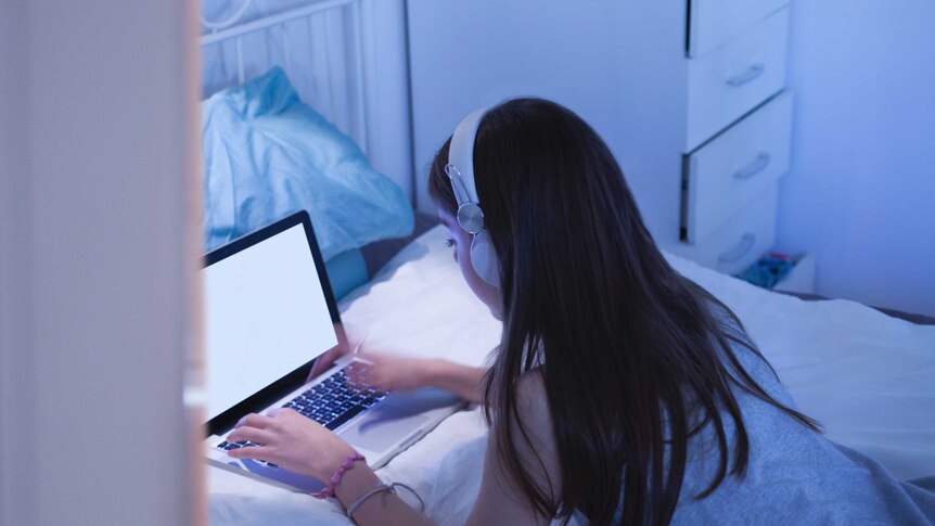 A girl lies on a bed and look at her computer.