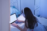 A girl lies on a bed and look at her computer.