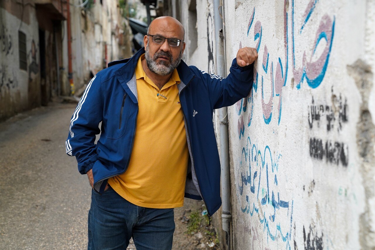 A man looking at the camera, and leaning against a wall