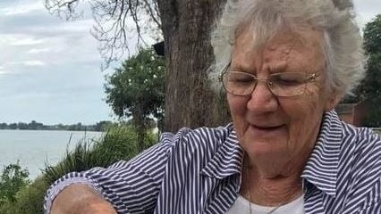 An elderly woman looks down as she grabs hold of a hamburger.