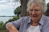 An elderly woman looks down as she grabs hold of a hamburger.