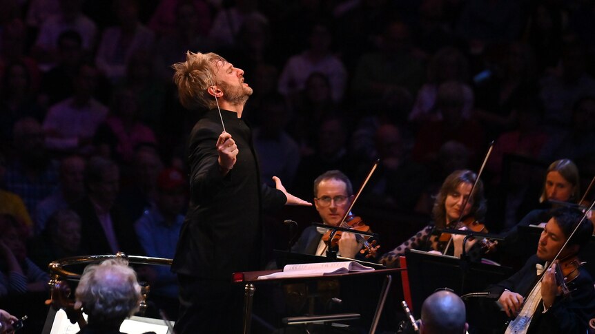 Conductor Kirill Karabits, arms raised, in full baton flight leading the Bournemouth Symphony Orchestra.