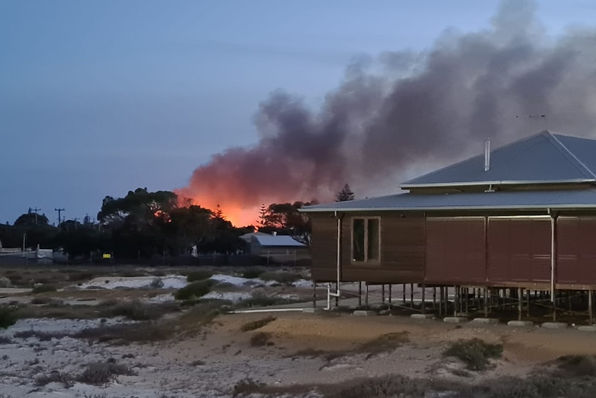 A fire burns beyond a home in a coastal town