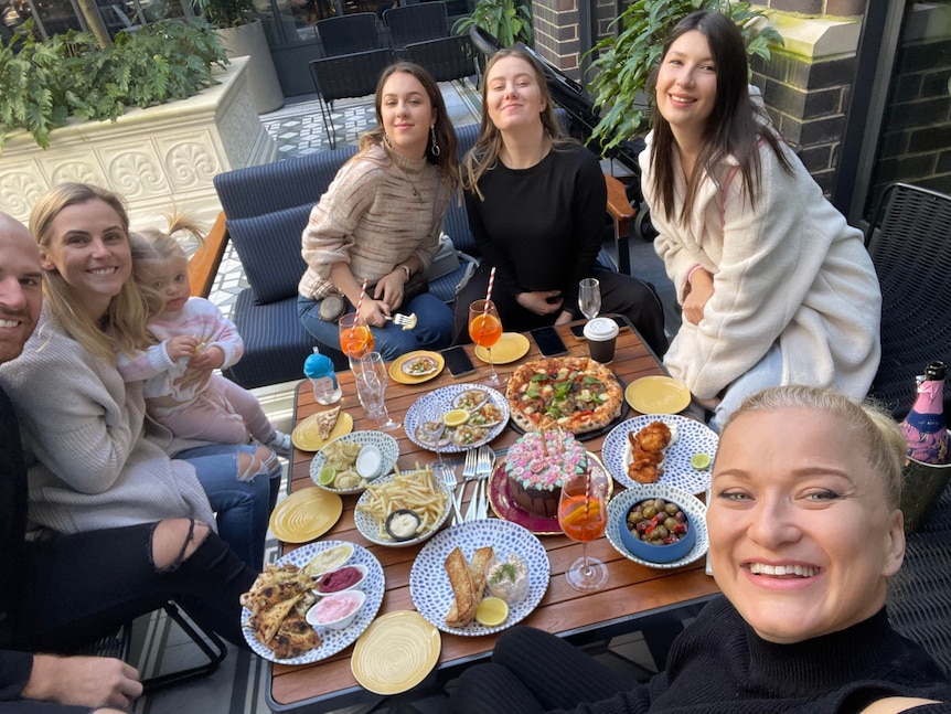 Friends and family sit around a table laid with lots of food to celebrate a birthday