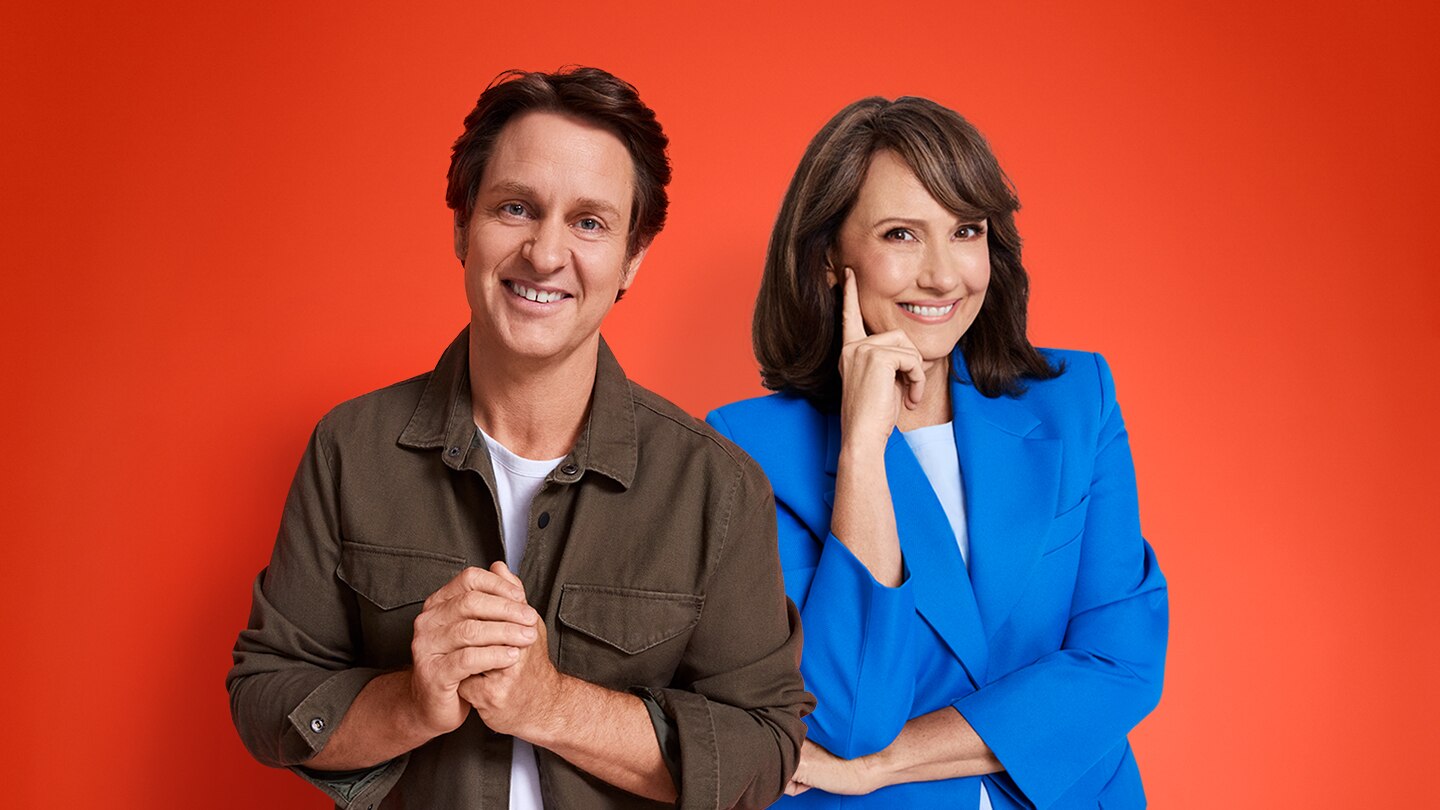 Craig Reucassel and Chris Bath smiling in front of a red background.