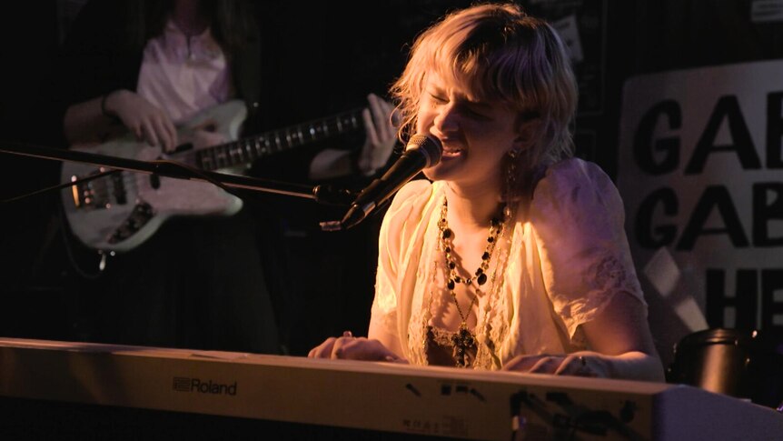 Musician Ruby Archer performing with a band in low light singing and playing keyboard 