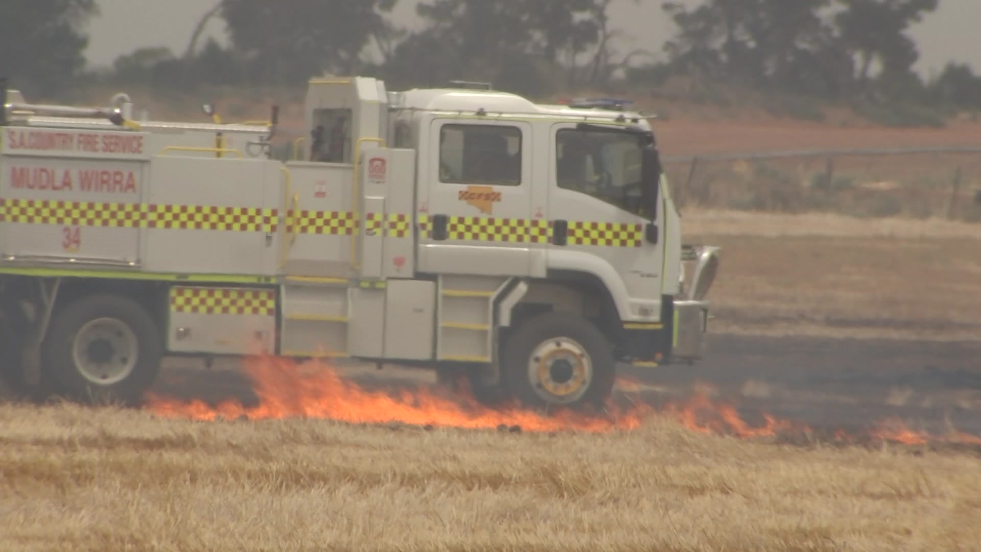 A firetruck next to a small grass fire in a paddock
